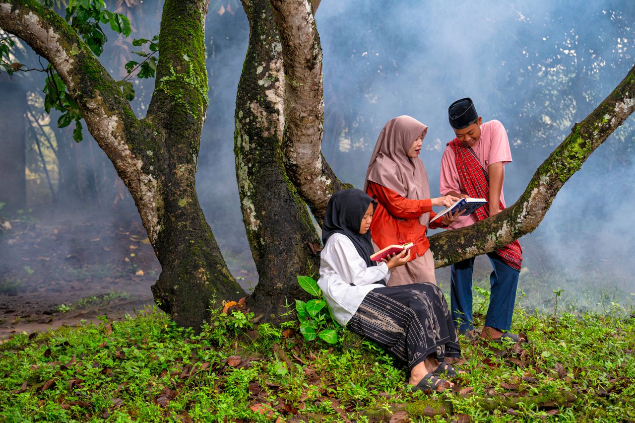 Indonesian teens reading together in a serene outdoor setting, promoting education and culture.
