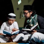 A father and son reading religious texts on the floor in a mosque, fostering learning and connection.